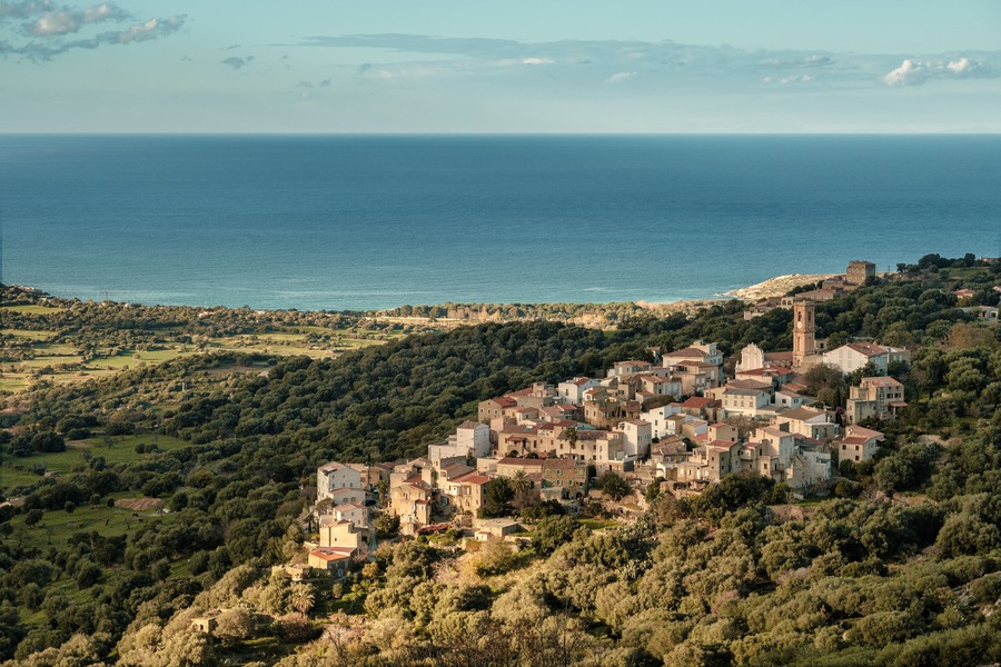 The ancient mountain village of Aregno lit by the afternoon sun and surrounded by autumnal trees in the Balagne region of Corsica with the Mediterranean see in the distance