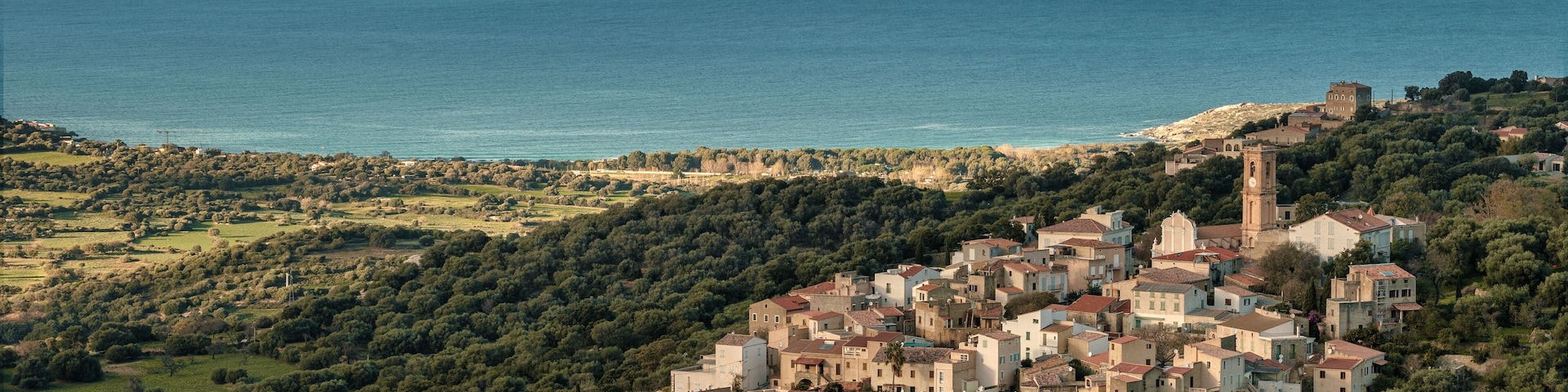 The ancient mountain village of Aregno lit by the afternoon sun and surrounded by autumnal trees in the Balagne region of Corsica with the Mediterranean see in the distance