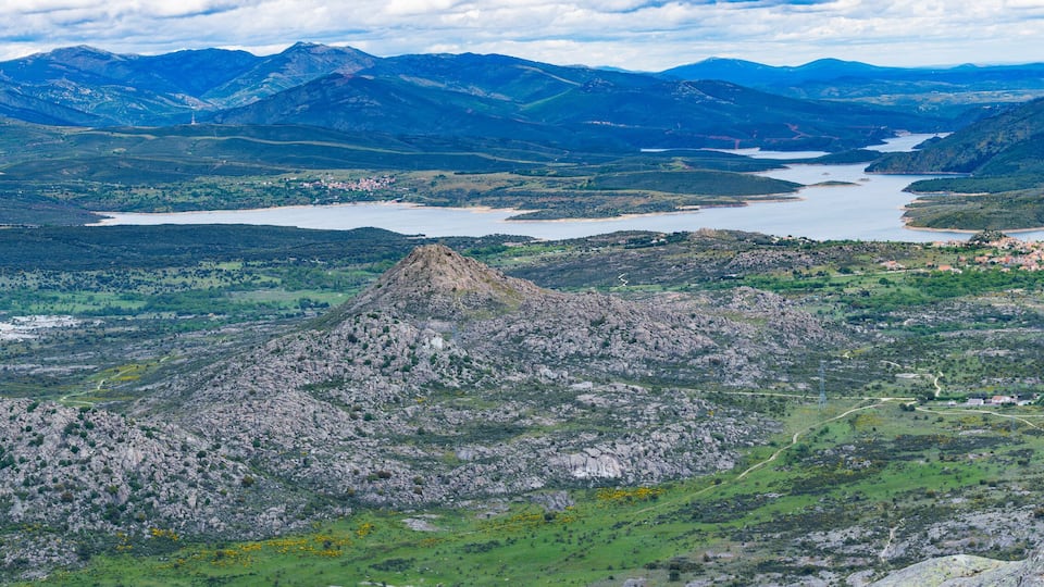 A mountainous landscape with a lake, a prominent rocky peak, and a small village.