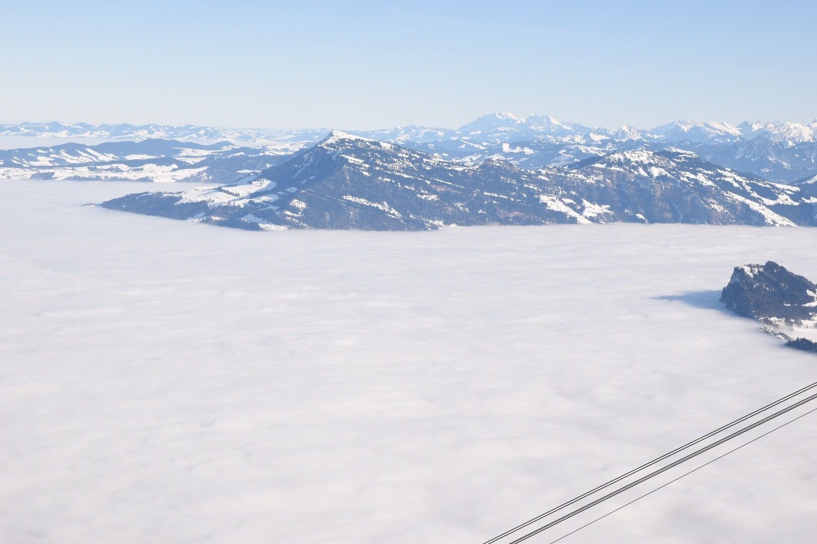 Paisagem montanhosa com picos cobertos de neve e uma camada de nuvens abaixo.