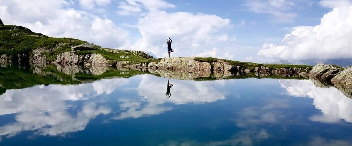 A person meditating on a rock by a calm lake with a clear reflection.