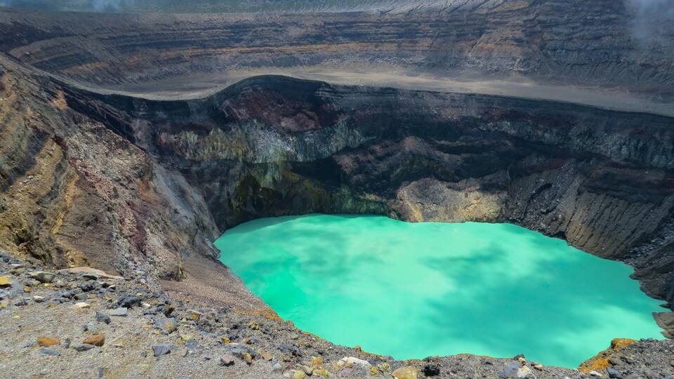 A large crater with turquoise water surrounded by rugged terrain.