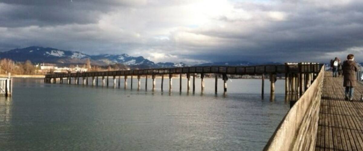 A wooden pier extending into a calm body of water with mountains in the background.