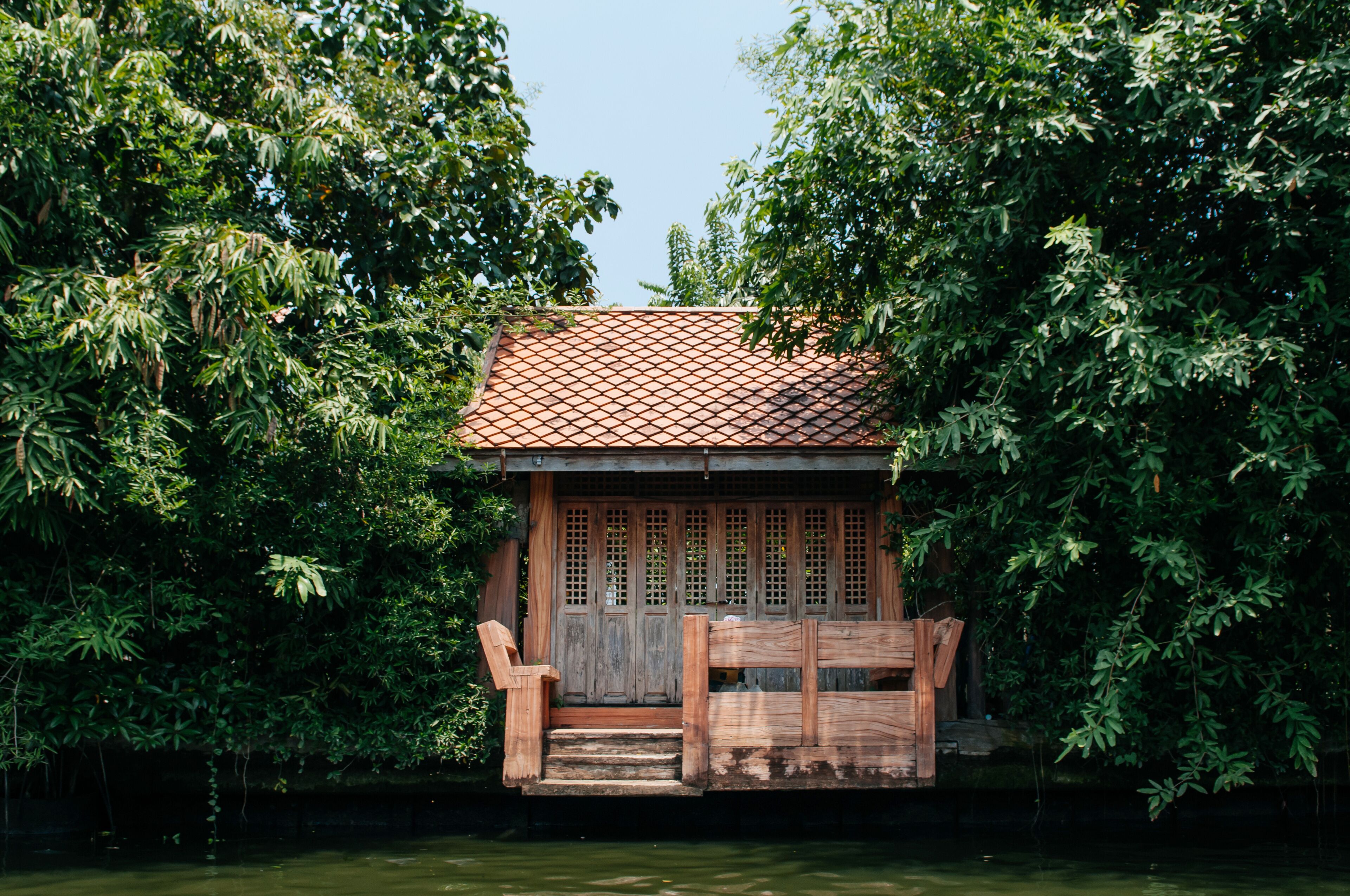 A wooden house with a tiled roof surrounded by lush greenery.