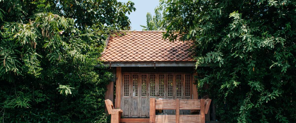 A wooden house with a tiled roof surrounded by lush greenery.