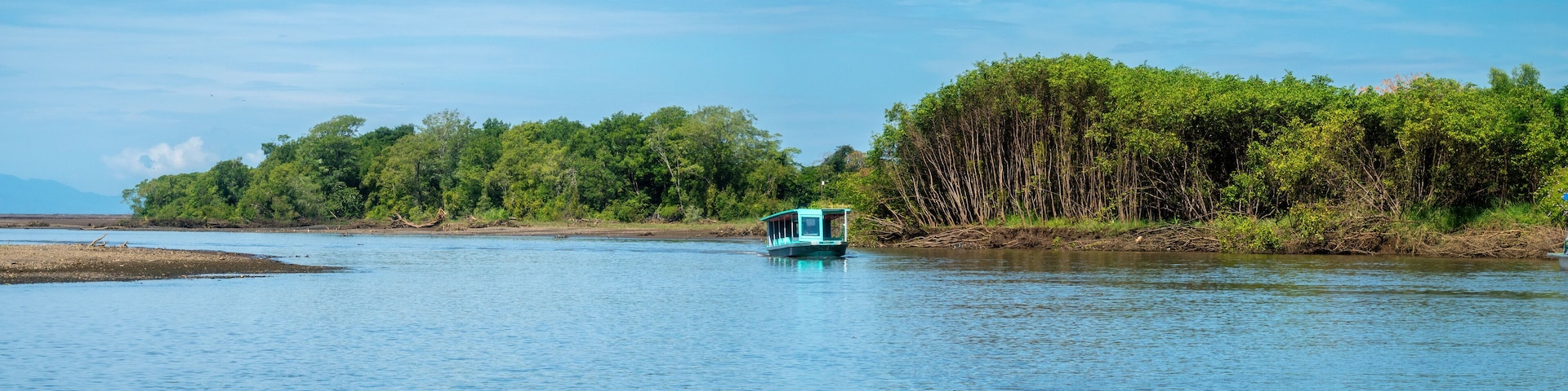 A calm river with a small boat in the center, surrounded by dense green foliage and a clear blue sky.