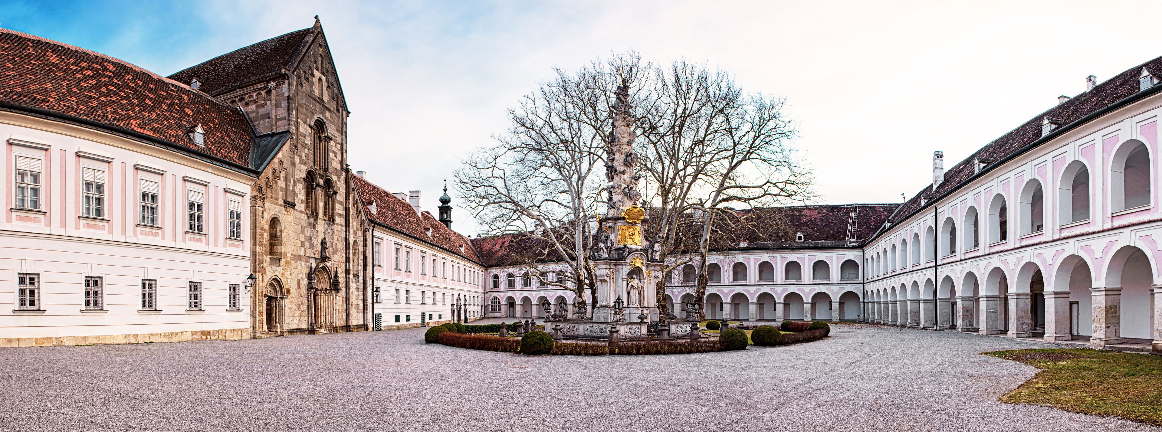 A courtyard with a fountain, a church, and a building with arched windows.