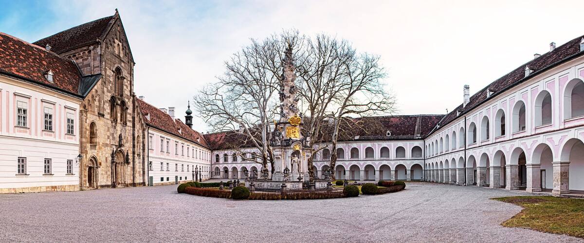 A courtyard with a fountain, a church, and a building with arched windows.