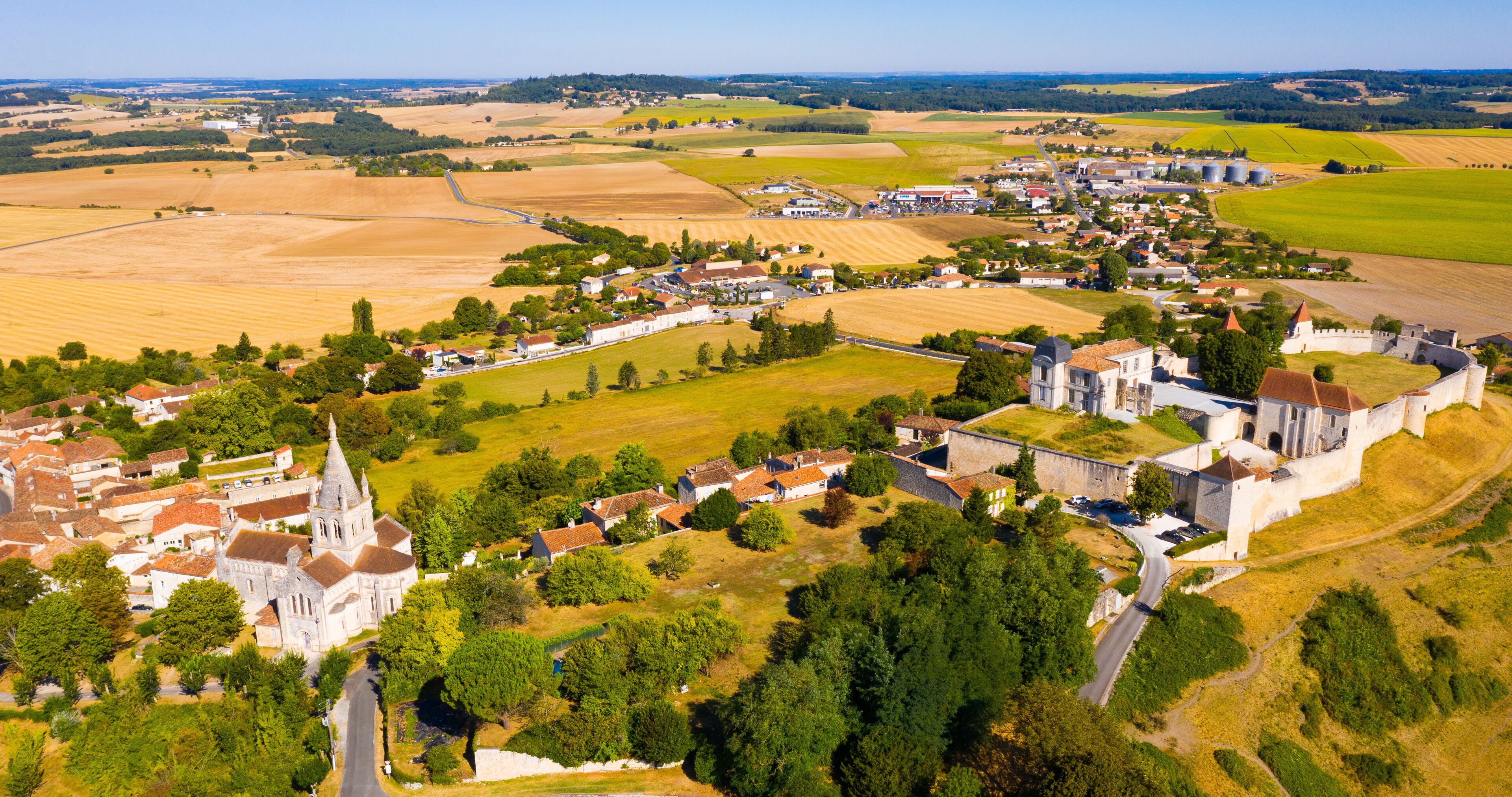 An aerial view of a historic town with a prominent church, castle, and surrounding agricultural fields.
