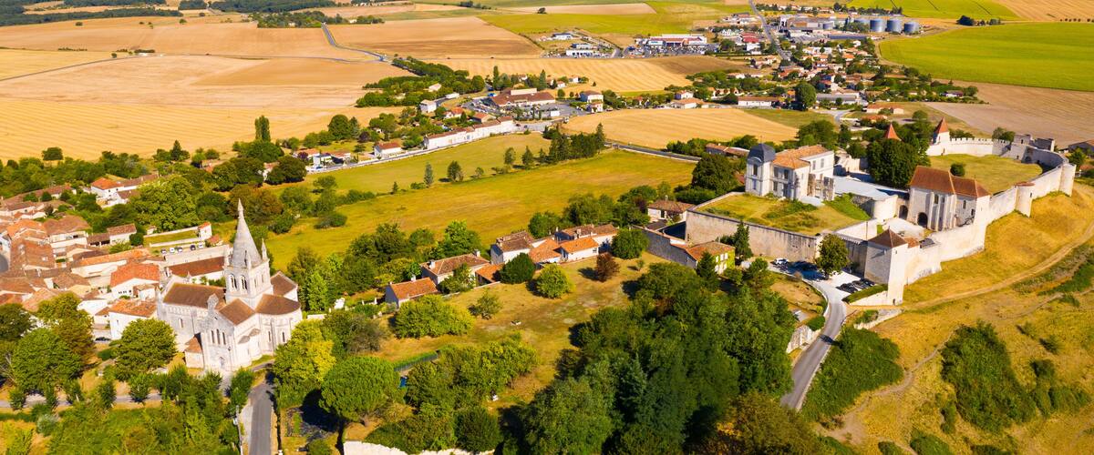 An aerial view of a historic town with a prominent church, castle, and surrounding agricultural fields.