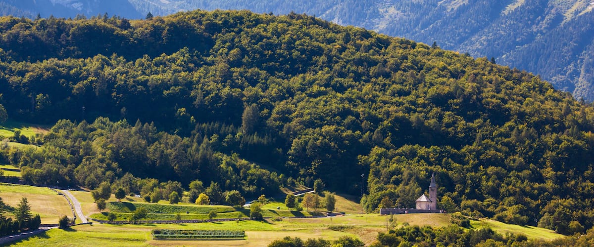 A mountainous landscape with a church on a hill, surrounded by lush greenery and clear skies.