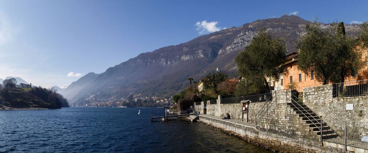 A coastal town with a stone staircase leading to a waterfront, a small island in the background, and mountains.