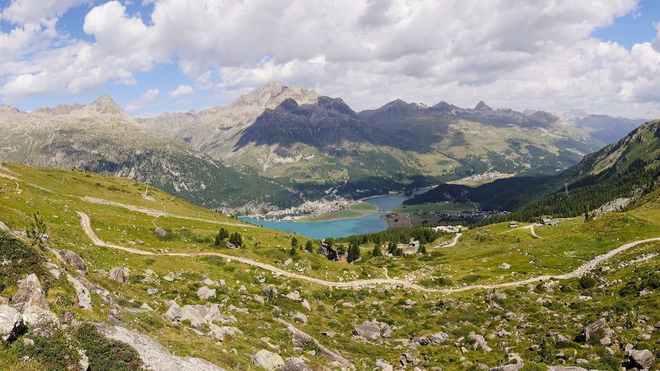 A mountainous landscape with a lake, winding paths, and rocky terrain.