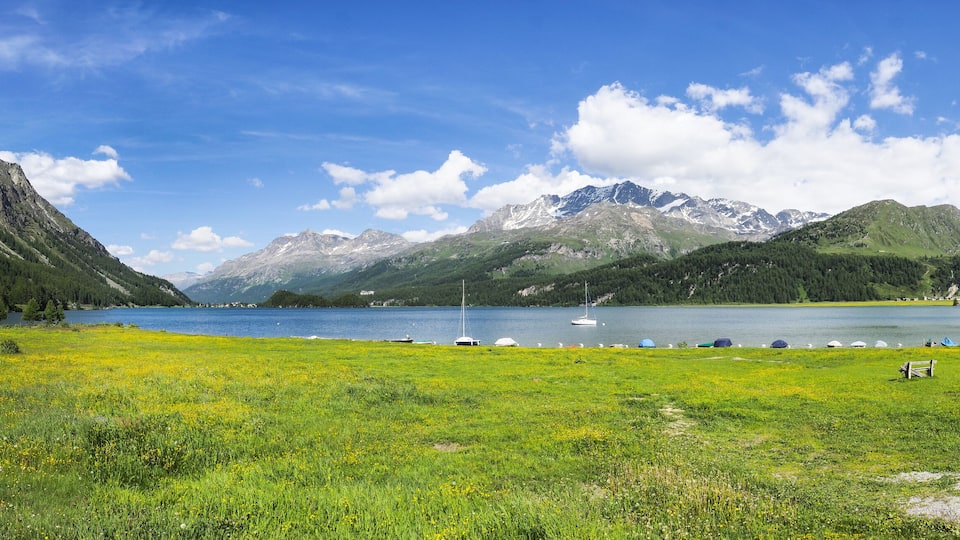A mountain landscape with a lake, boats, and a bench.
