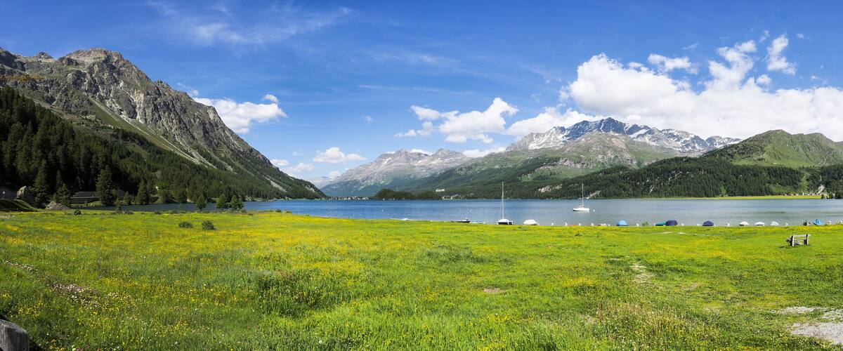 A mountain landscape with a lake, boats, and a bench.