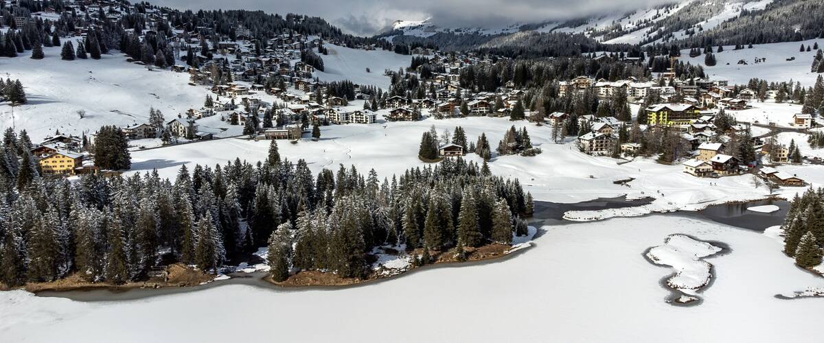 Un villaggio montano imbiancato dalla neve, circondato da fitti boschi e attraversato da un fiume.