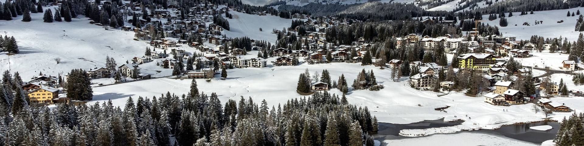 Un pueblo en la montaña cubierto de nieve, con bosques densos y un río.