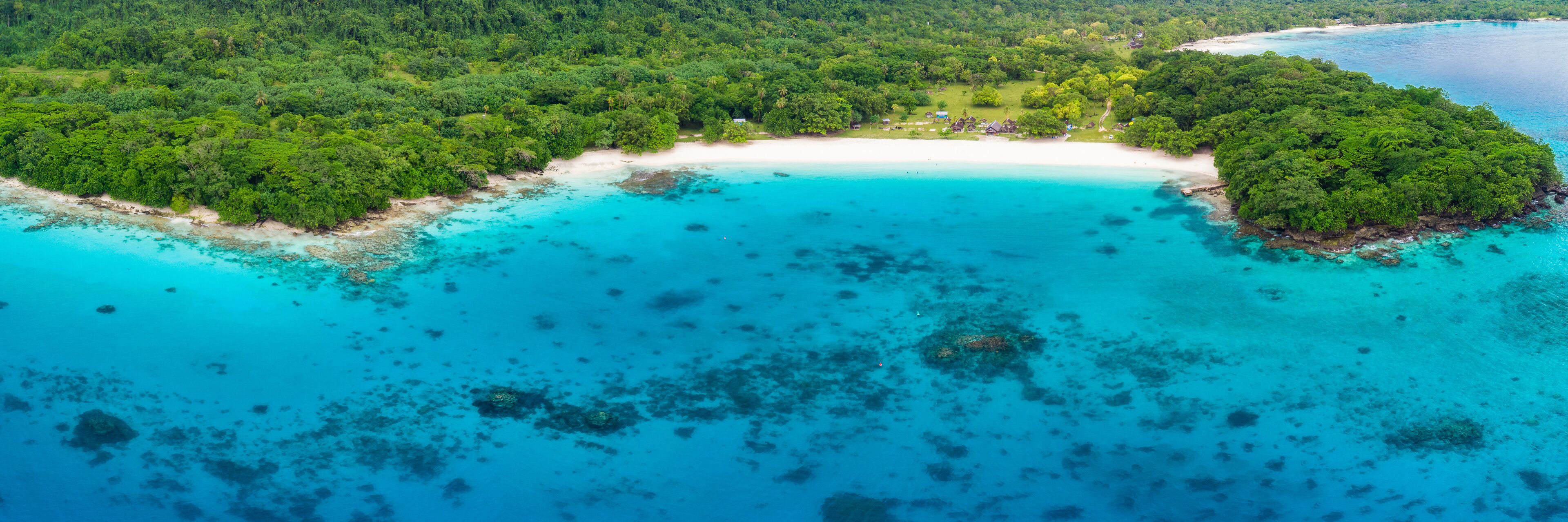 An aerial view of a tropical island with a white sandy beach, turquoise waters, and dense green forest.