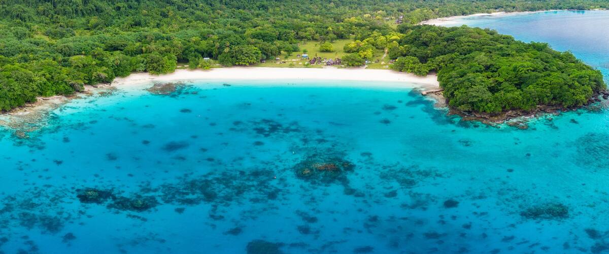 An aerial view of a tropical island with a white sandy beach, turquoise waters, and dense green forest.