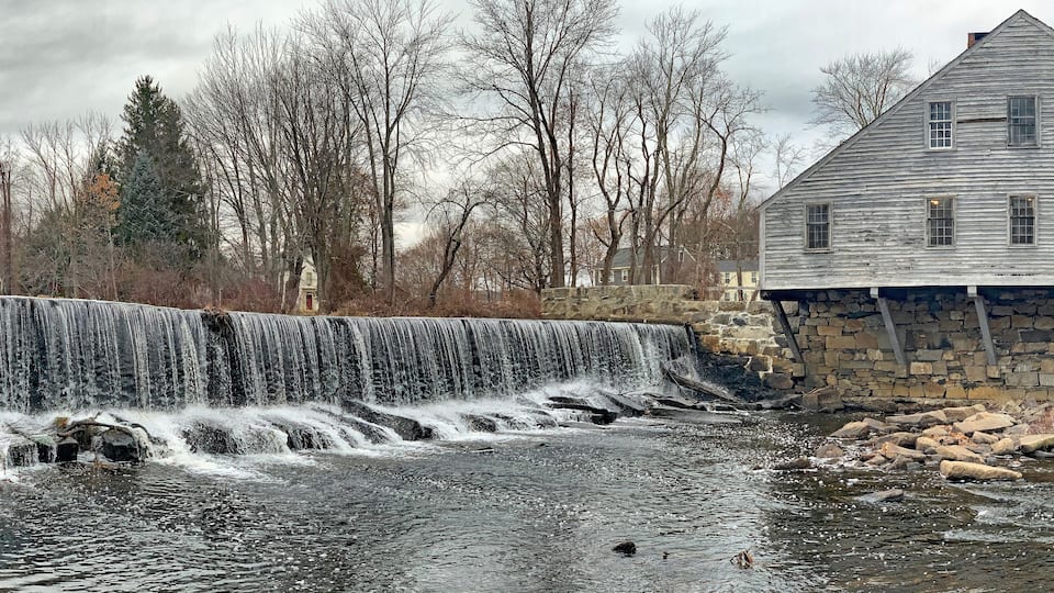 A waterfall, a stone building, and leafless trees.