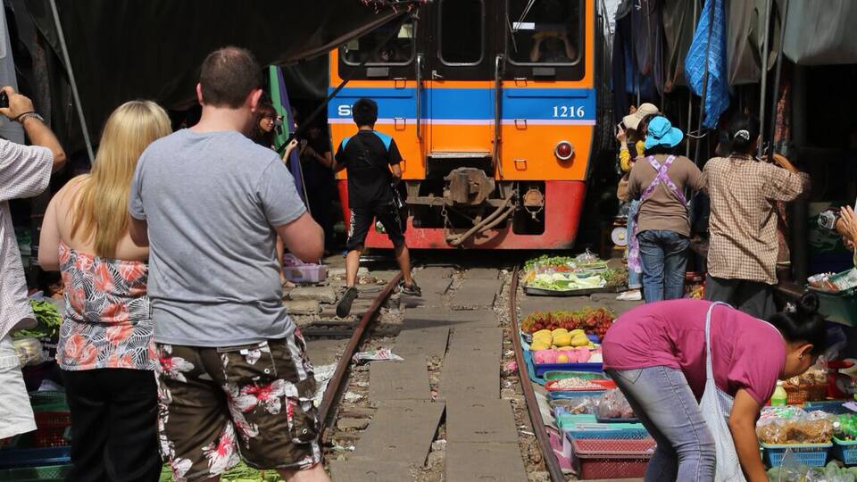 A train on tracks with people and produce stalls nearby.