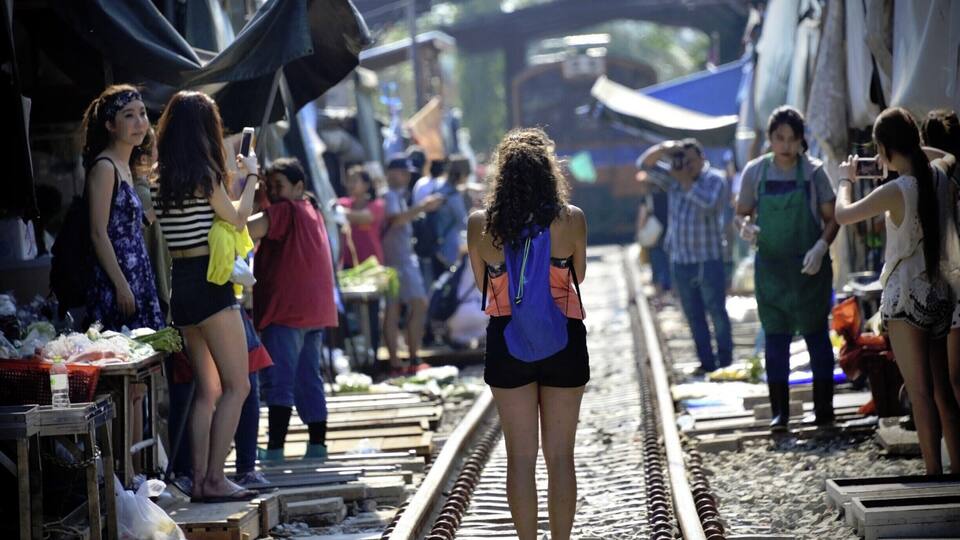 A crowded market area with people standing on train tracks.