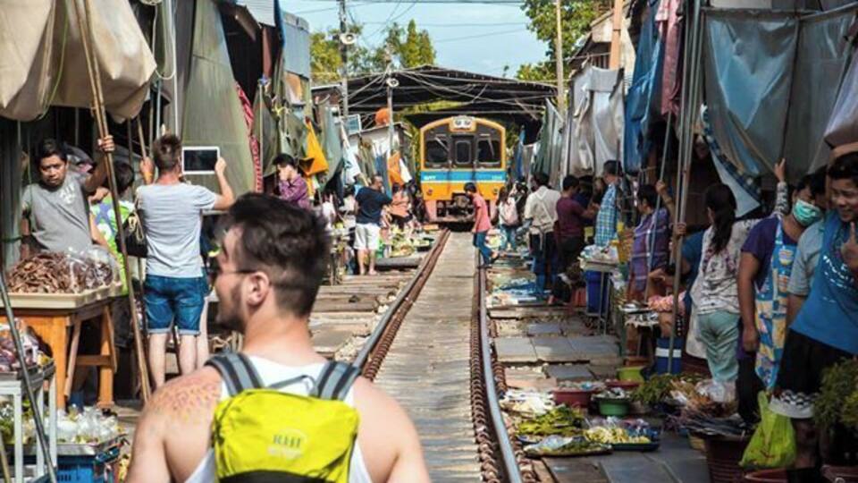 A person with a backpack walking on train tracks with a train in the background.