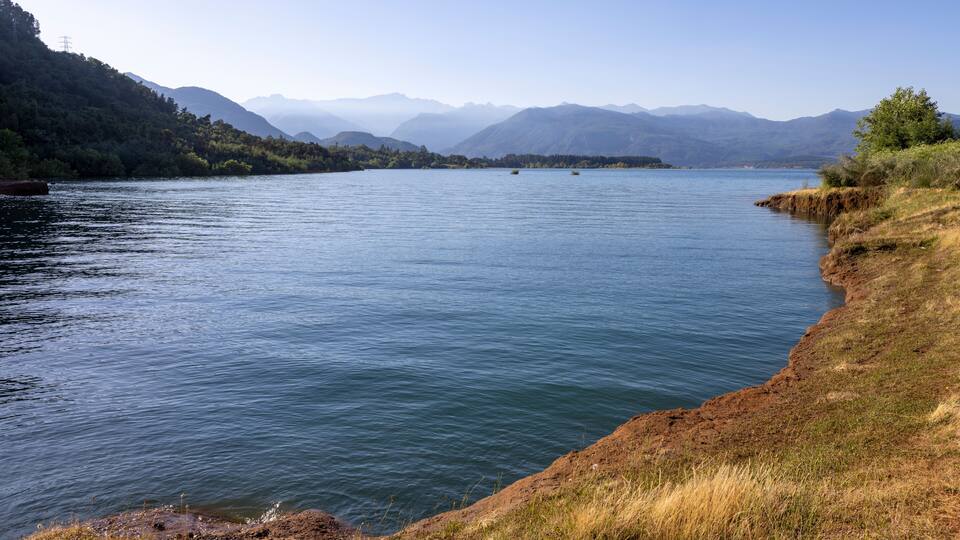 A calm lake with mountains in the background and a grassy shoreline.
