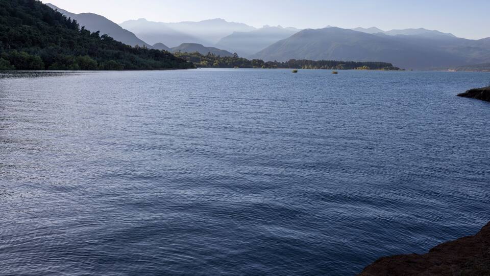 A calm lake surrounded by mountains and dense forest.