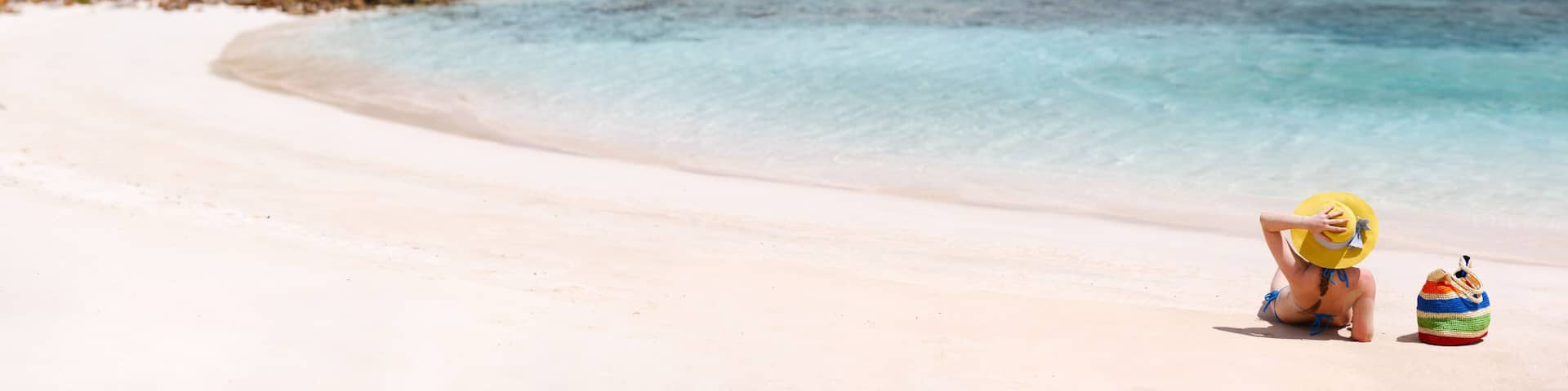 A beach with clear turquoise water, a sandy shore, and a small island in the distance.