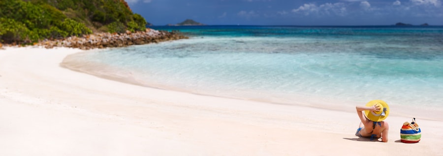 Uma praia com águas turquesa cristalinas, areal arenoso e uma pequena ilha ao longe.
