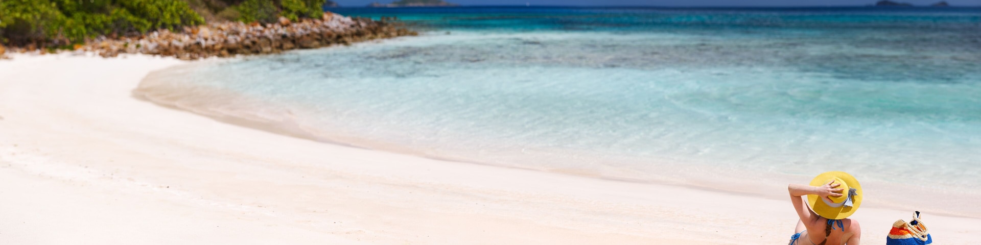 Uma praia com águas turquesa cristalinas, areal arenoso e uma pequena ilha ao longe.