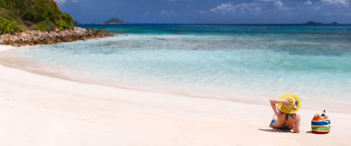 A beach with clear turquoise water, a sandy shore, and a small island in the distance.