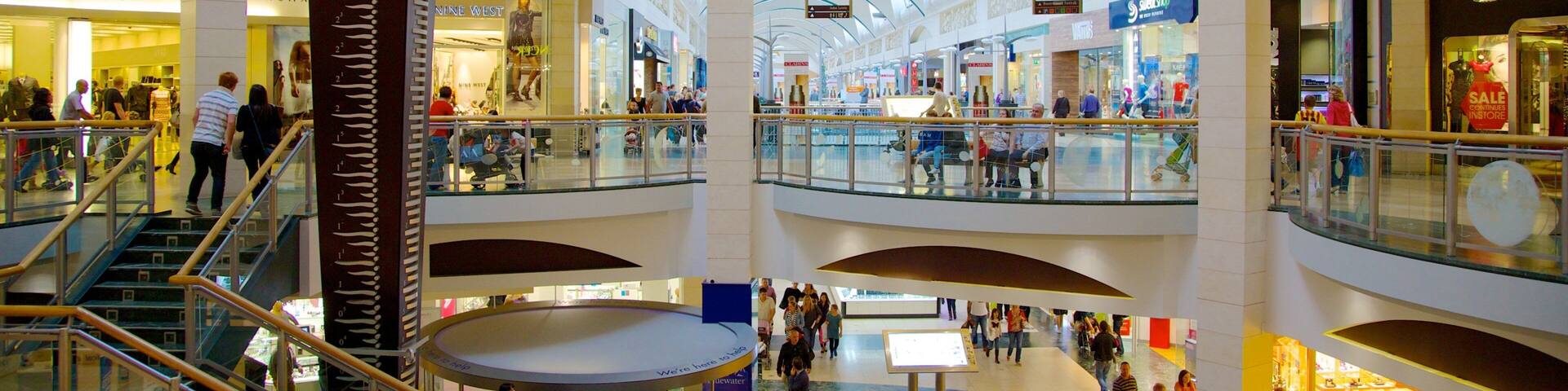 Un centre commercial à plusieurs niveaux, doté de rampes en verre, d’escalators et de nombreux magasins.