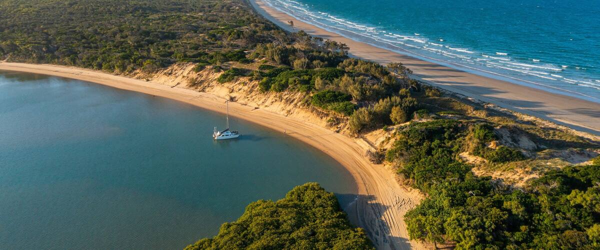 Un paysage côtier avec une plage de sable, un bateau sur l’eau et une végétation luxuriante.