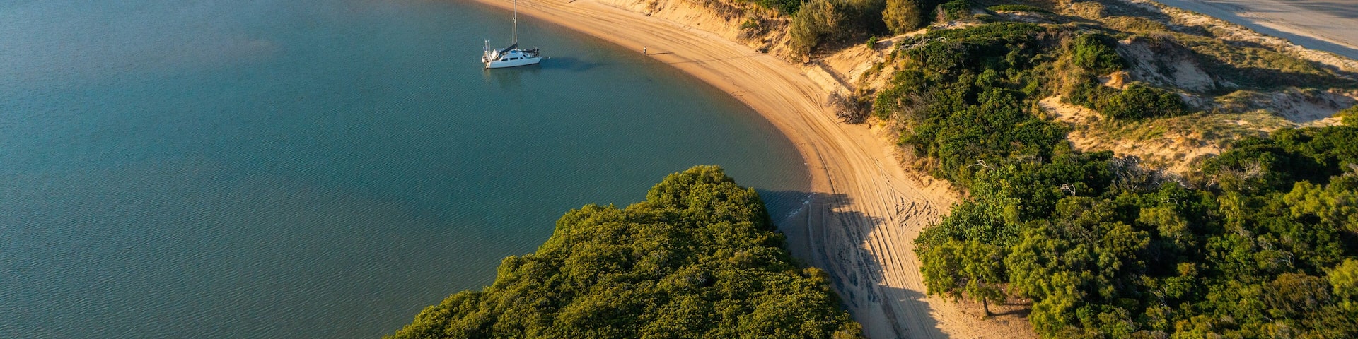 A coastal landscape with a sandy beach, a boat on the water, and dense greenery.