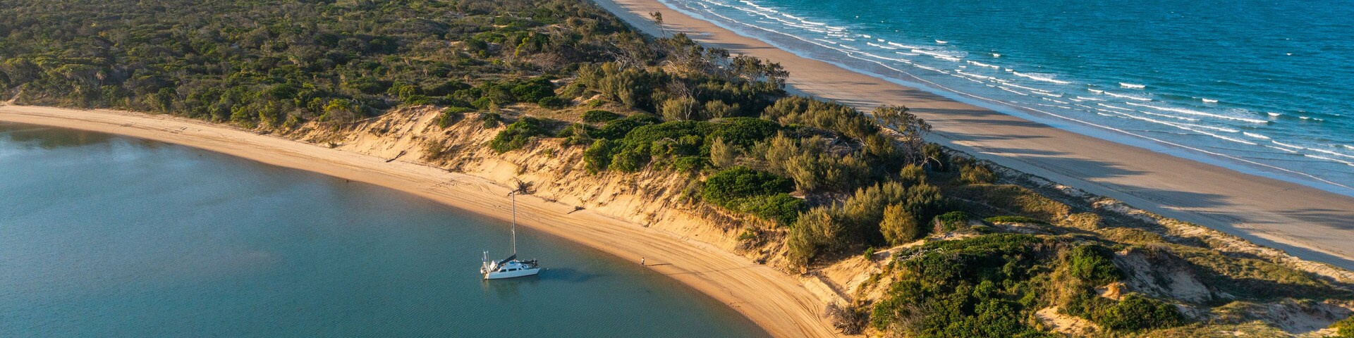 Un paysage côtier avec une plage de sable, un bateau sur l’eau et une végétation luxuriante.
