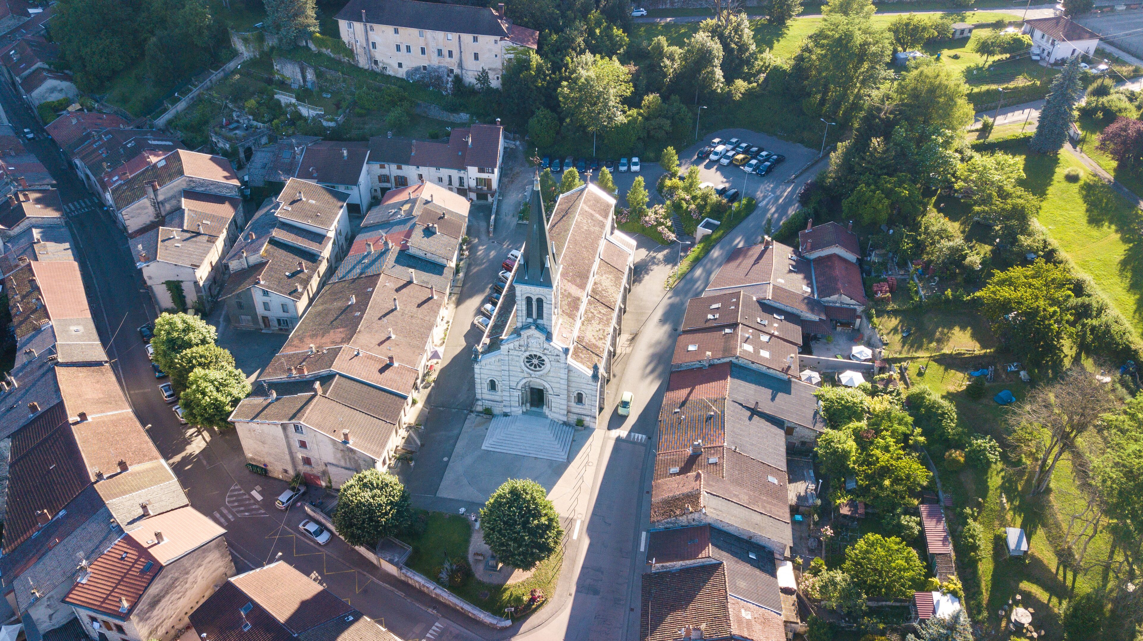 An aerial view of a historic town with a prominent church, narrow streets, and surrounding greenery.