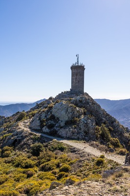 A rocky hill with a tower on top, surrounded by sparse vegetation and a clear sky.