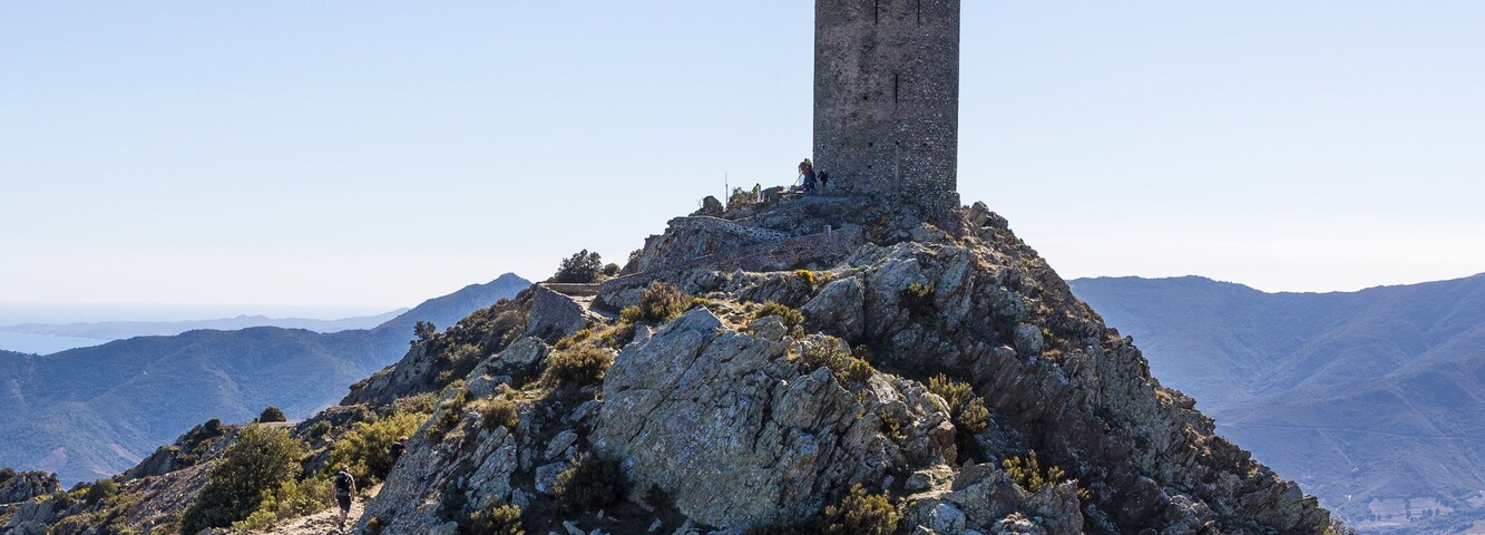 A rocky hill with a tower on top, surrounded by sparse vegetation and a clear sky.