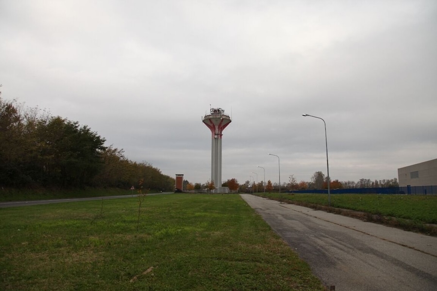 A tall tower with a red and white structure, surrounded by a grassy area and a paved road.