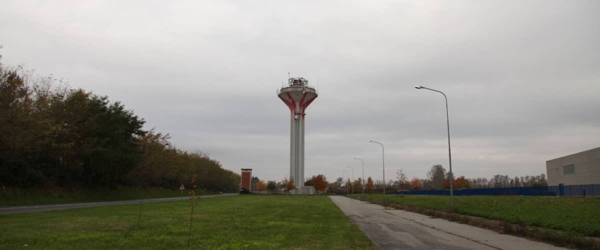 A tall tower with a red and white structure, surrounded by a grassy area and a paved road.