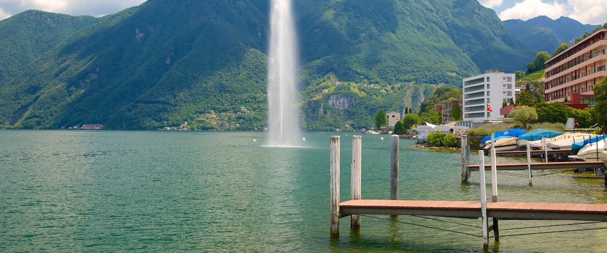 A lake with a fountain, mountains, and buildings.