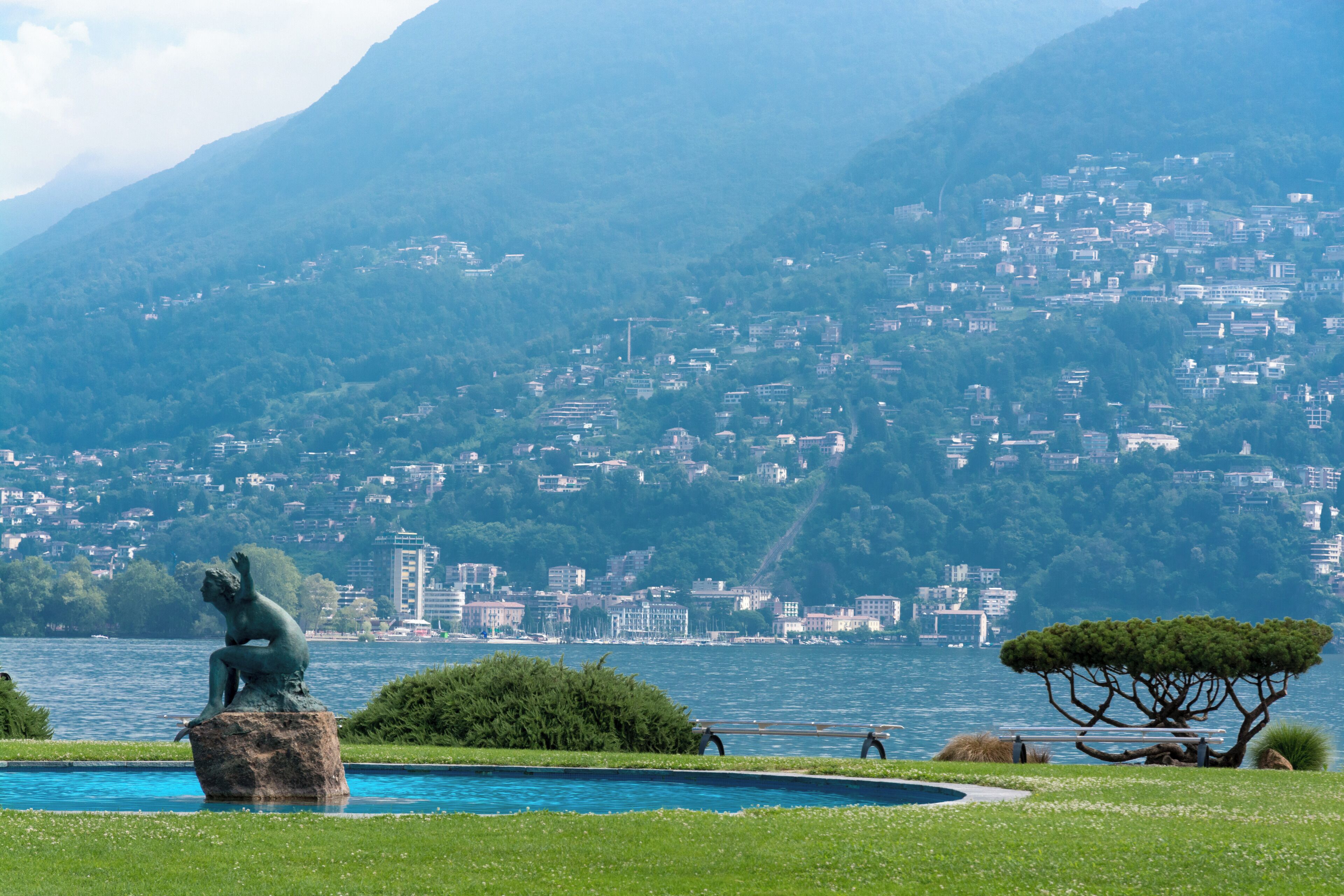 A statue by a pool with a lake and a town in the background.