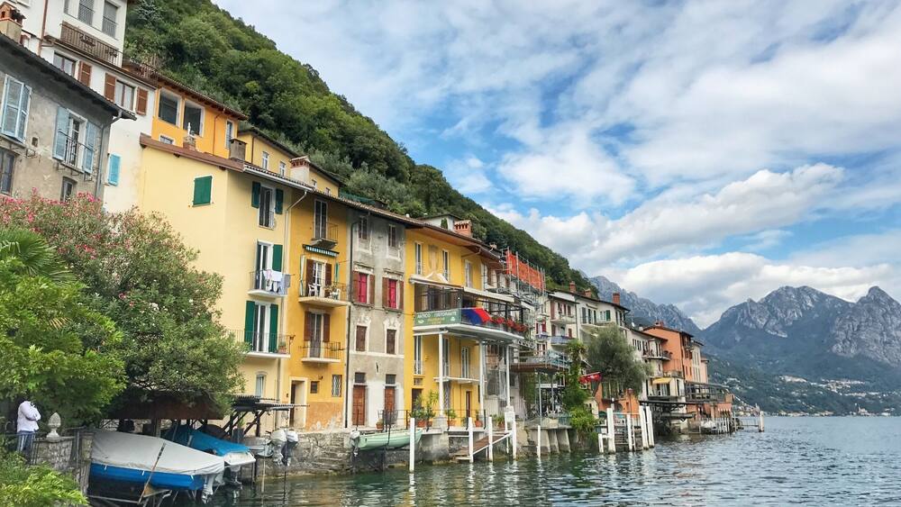 Un charmant village au bord d’un lac, avec ses bâtiments aux couleurs vives, ses bateaux et les montagnes qui se dressent à l’arrière-plan.