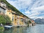 A picturesque lakeside village with colorful buildings, boats, and mountains in the background.