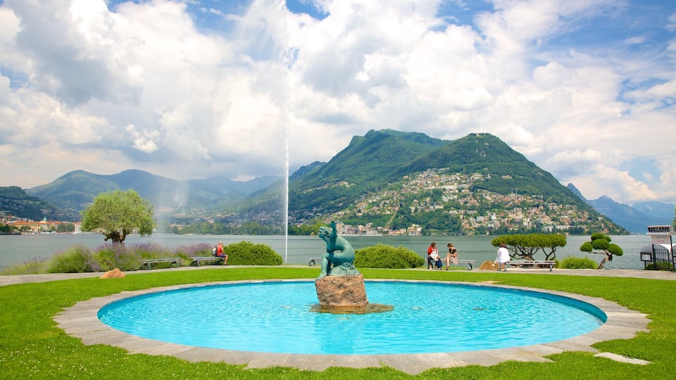 A swimming pool with a statue in the center, surrounded by greenery and a mountainous backdrop.