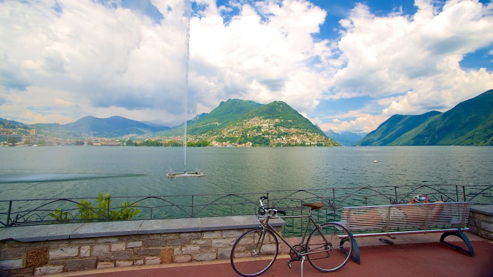 A lake with mountains in the background, a bench, and a bicycle.