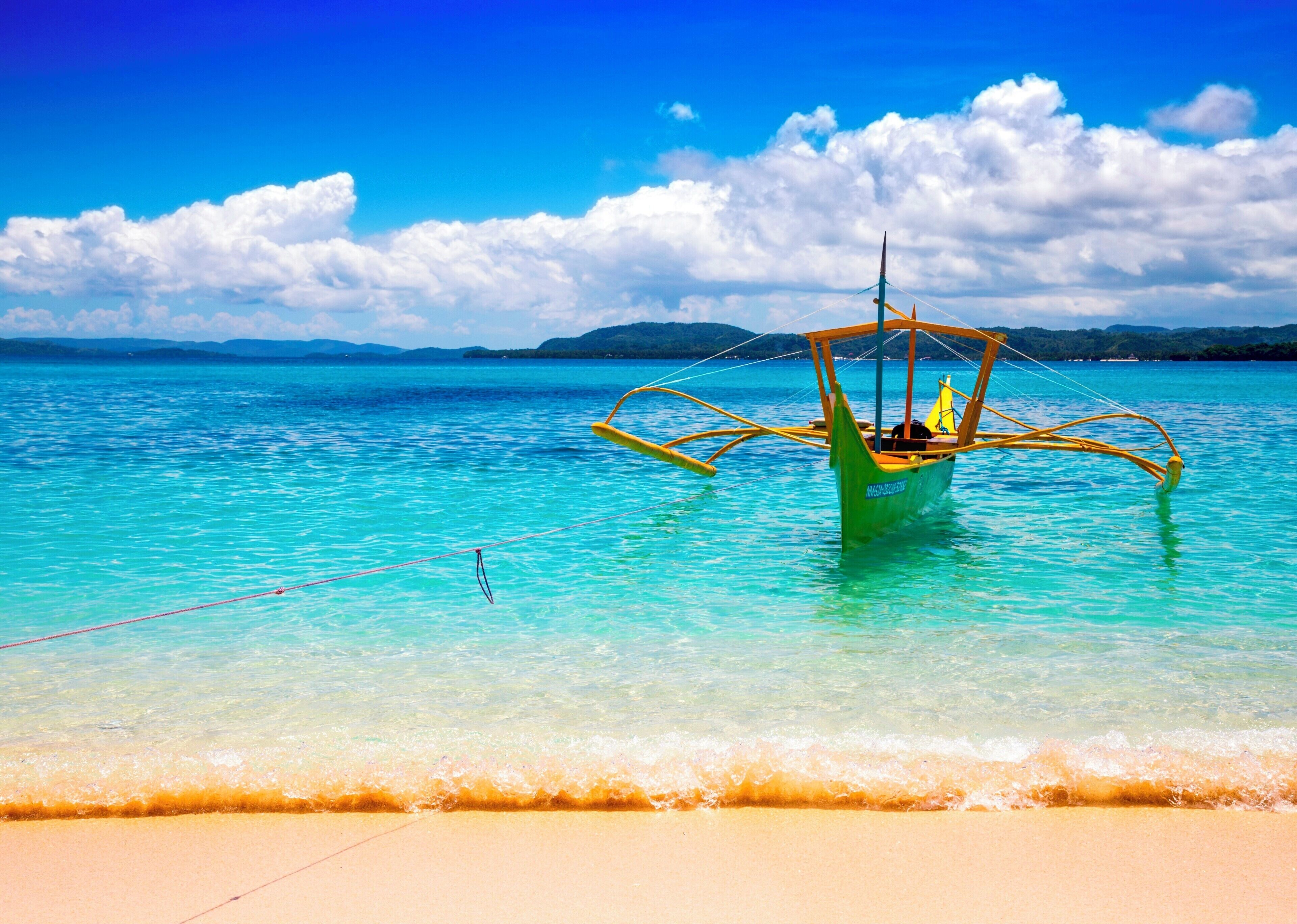 A traditional boat on a turquoise sea with clear skies and distant mountains.