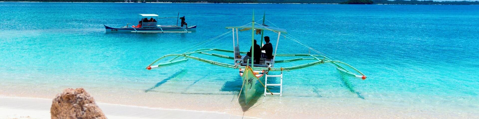A beach with clear turquoise water, a boat, and a wooden post in the foreground.